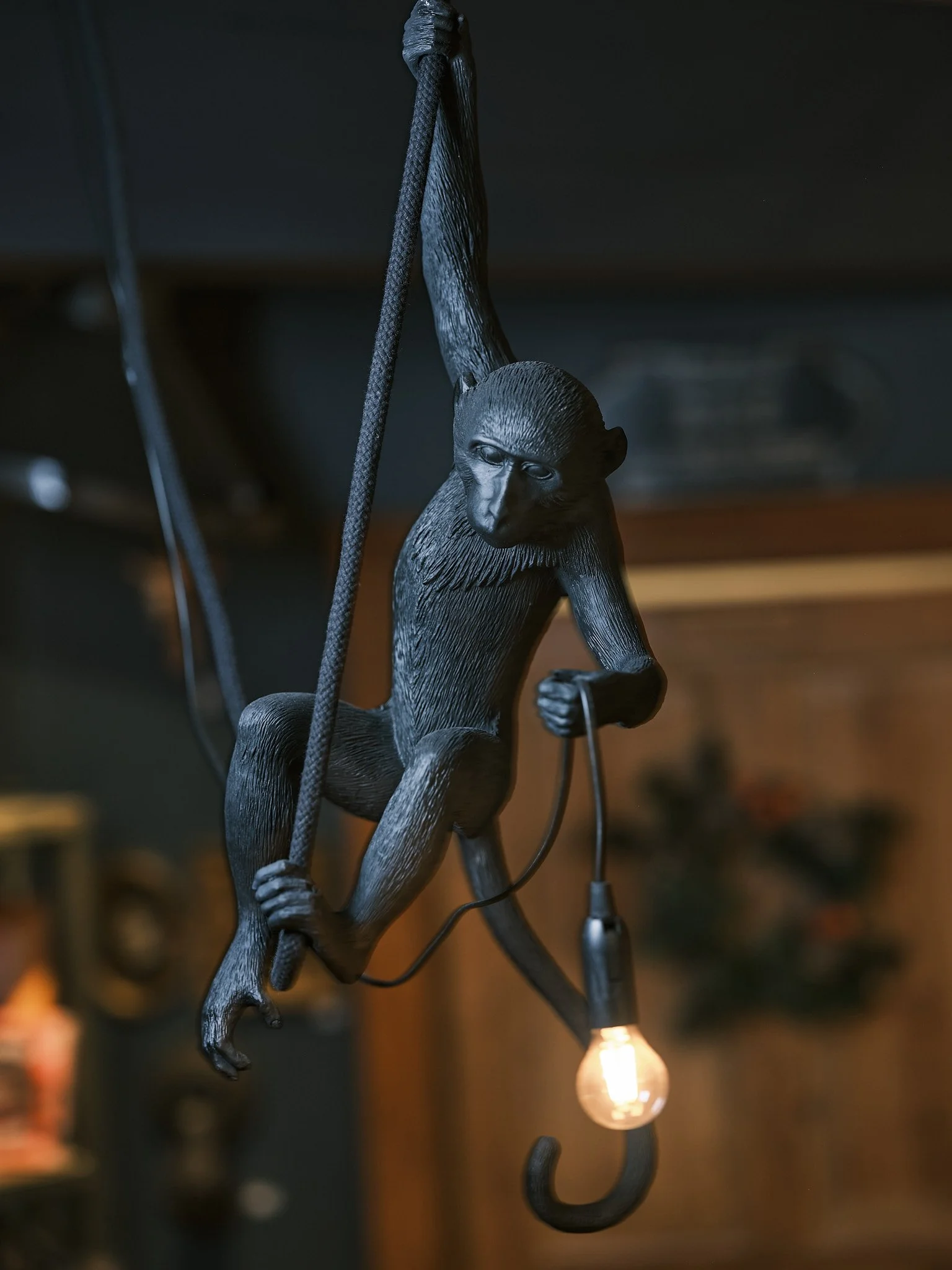 Skulptur av en apa som hänger i ett snöre och håller i ett glödande glödlampa med en krok.