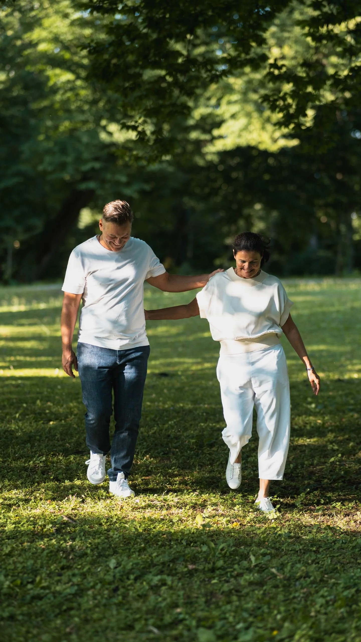 Zwei lächelnde Menschen, ein Mann und eine Frau, gehen gemeinsam im Park und scheinen sich zu amüsieren.