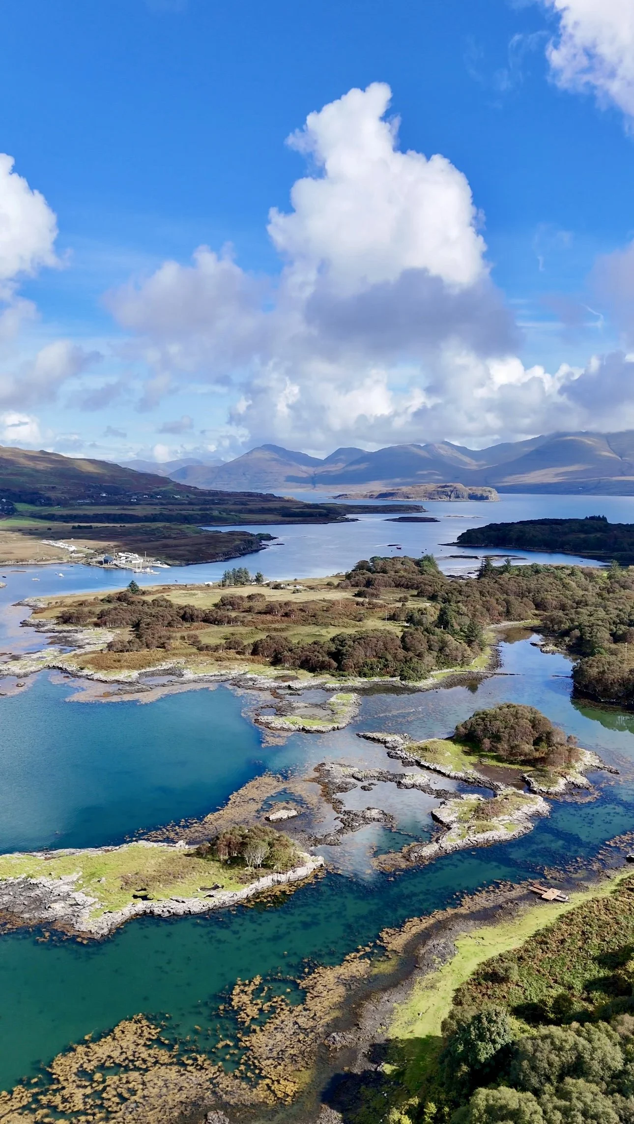 Aerial view of a landscape with a mix of lakes, islands, and land patches, surrounded by mountains and a cloudy sky.