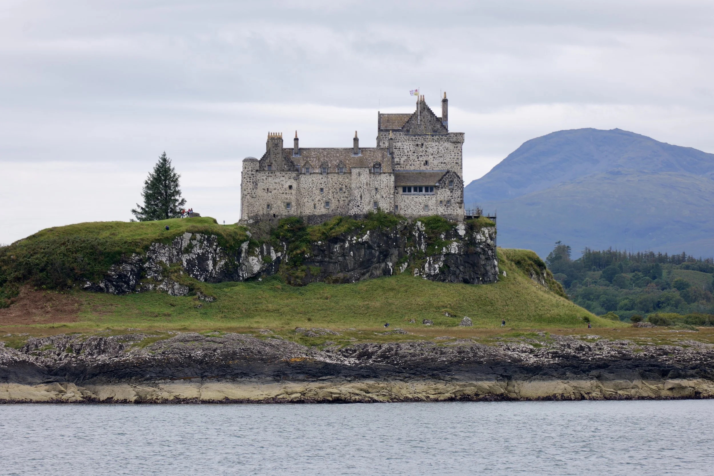 A historic castle on a rocky hill overlooking a body of water with a mountain in the background.