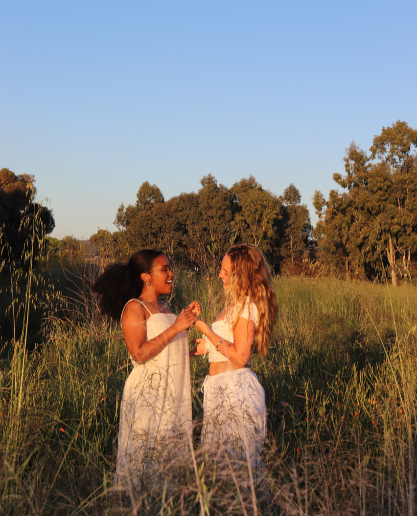 Women standing together in a sunlit field at golden hour, representing community, support, shared growth, and values-driven wellness and mindset coaching.