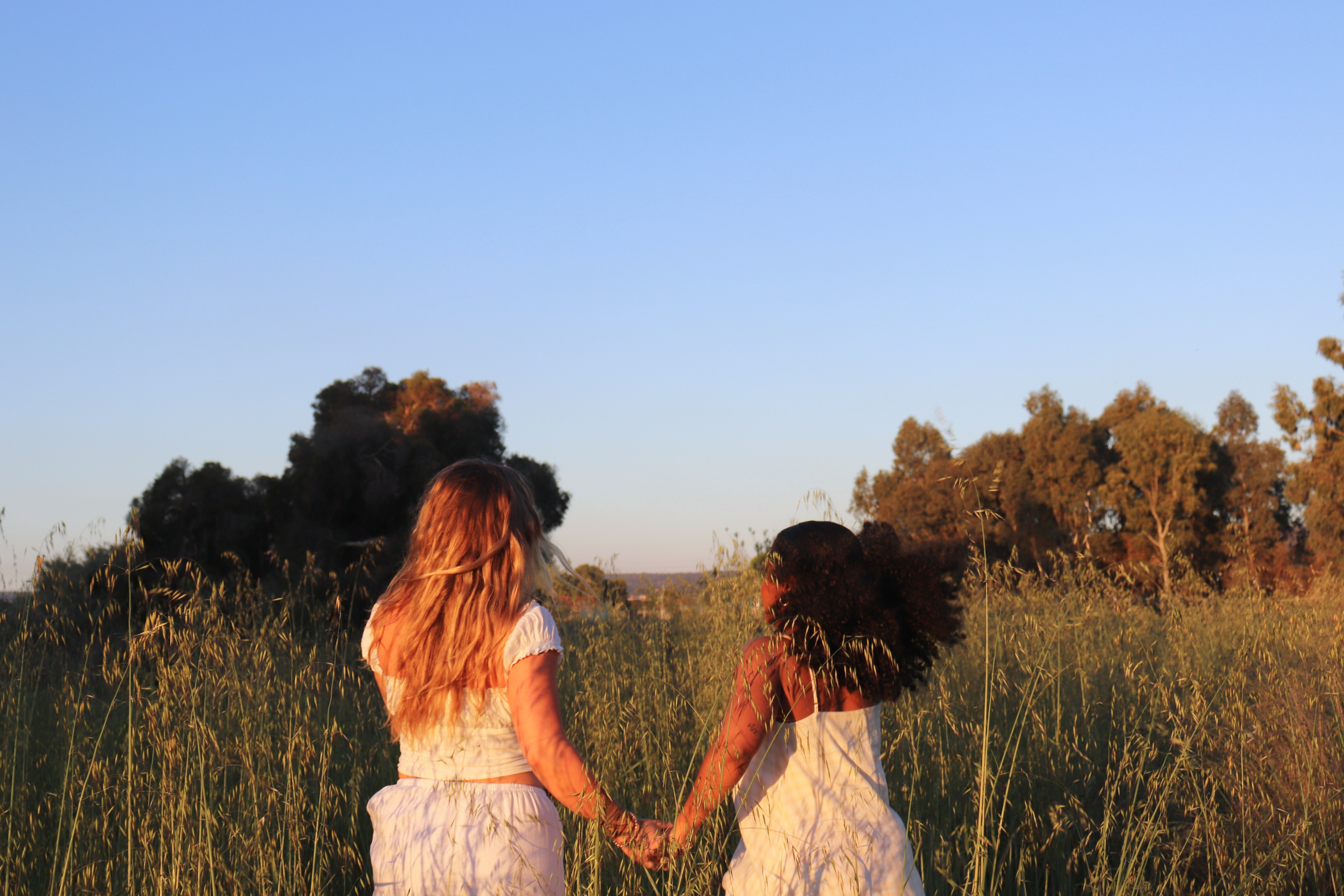 Two women holding hands while running through a field, symbolising trust, support, and taking confident steps forward with wellness and mindset coaching.