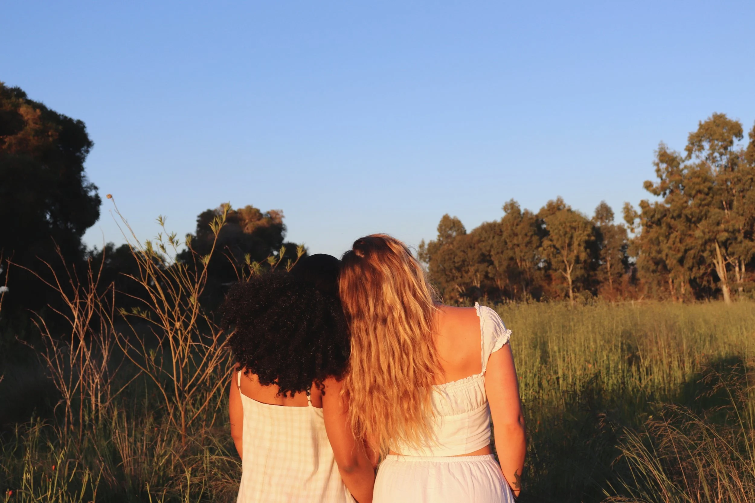 Two women standing side by side in a calm outdoor setting at sunset, reflecting connection, grounding, emotional wellbeing, and personal growth through mindset coaching.