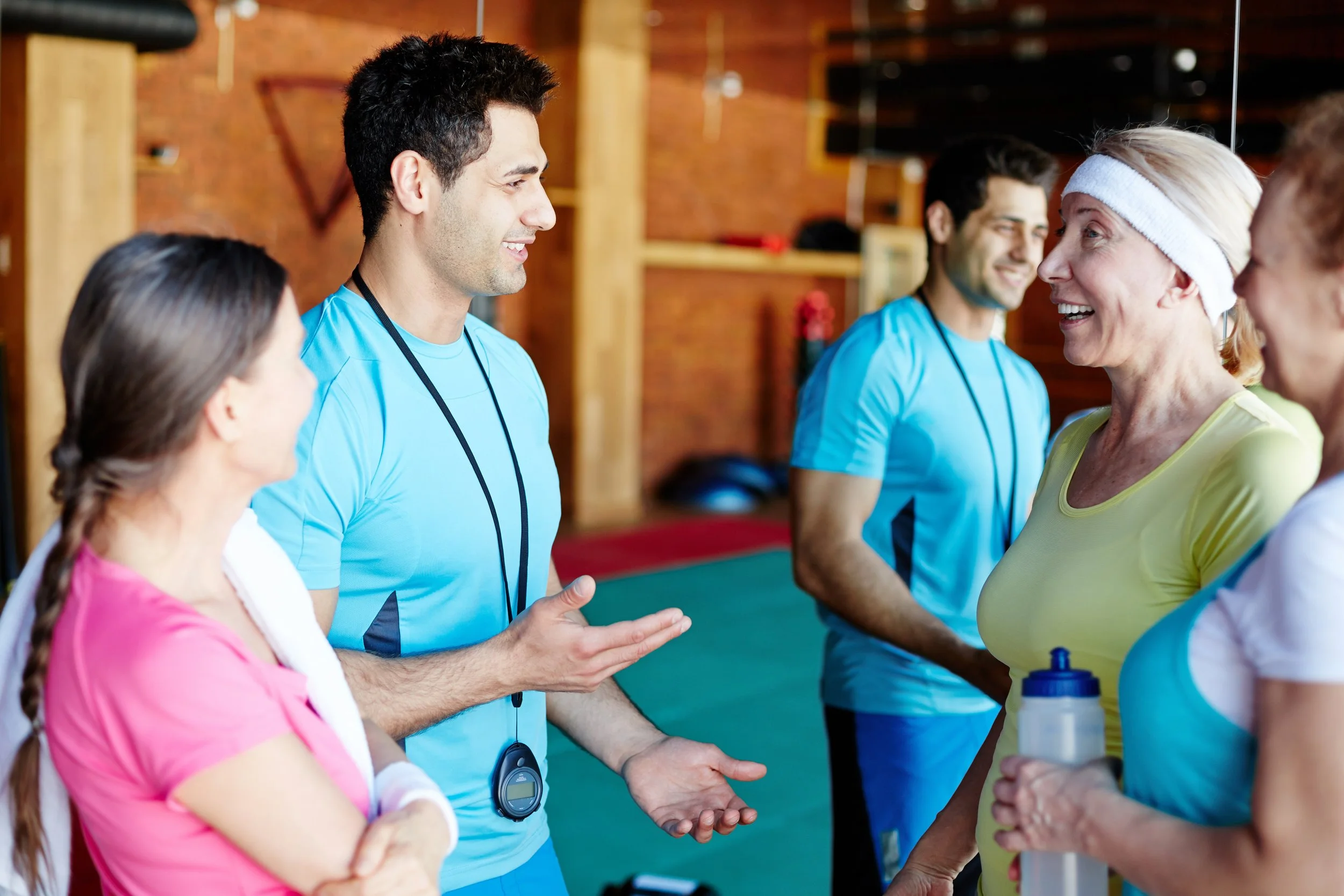 Group of people in workout attire chatting and smiling inside a gym or fitness studio.