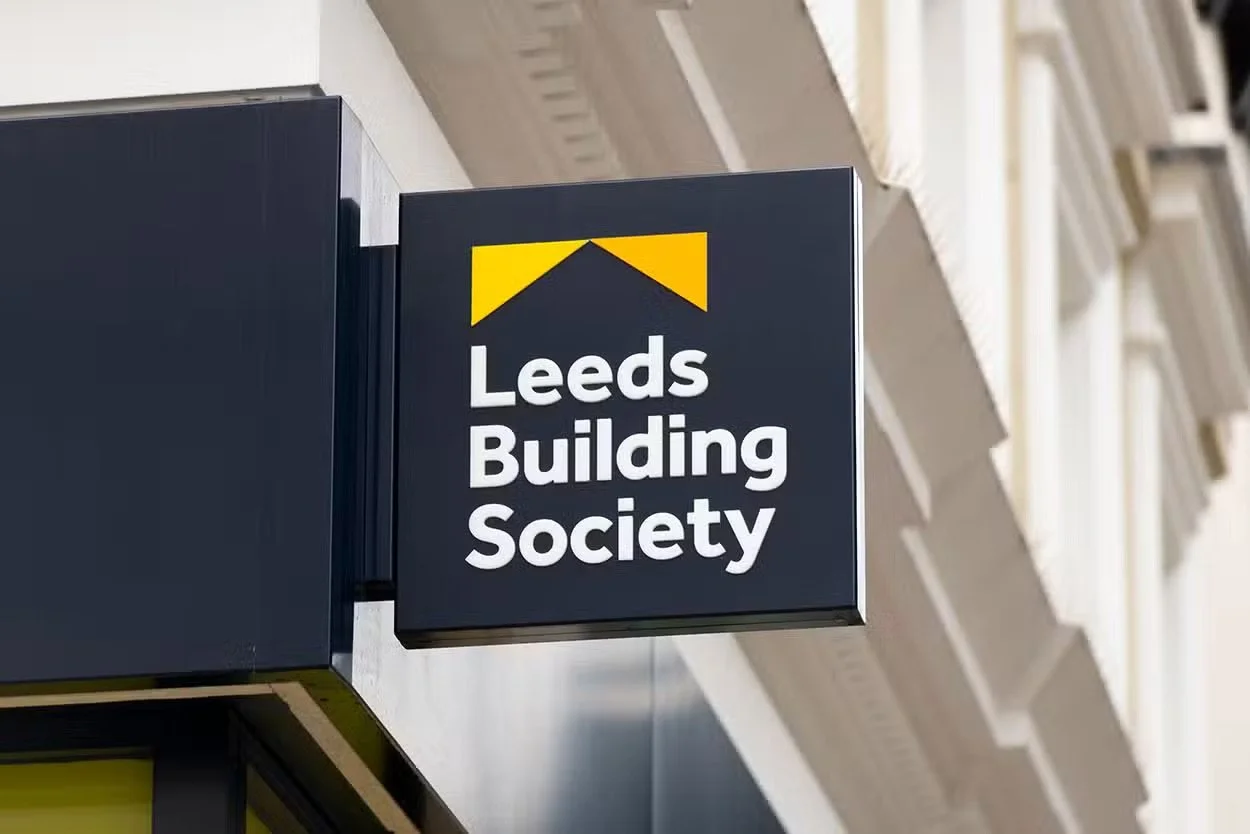 Sign for Leeds Building Society attached to a building facade, with a dark background and yellow geometric design at the top.