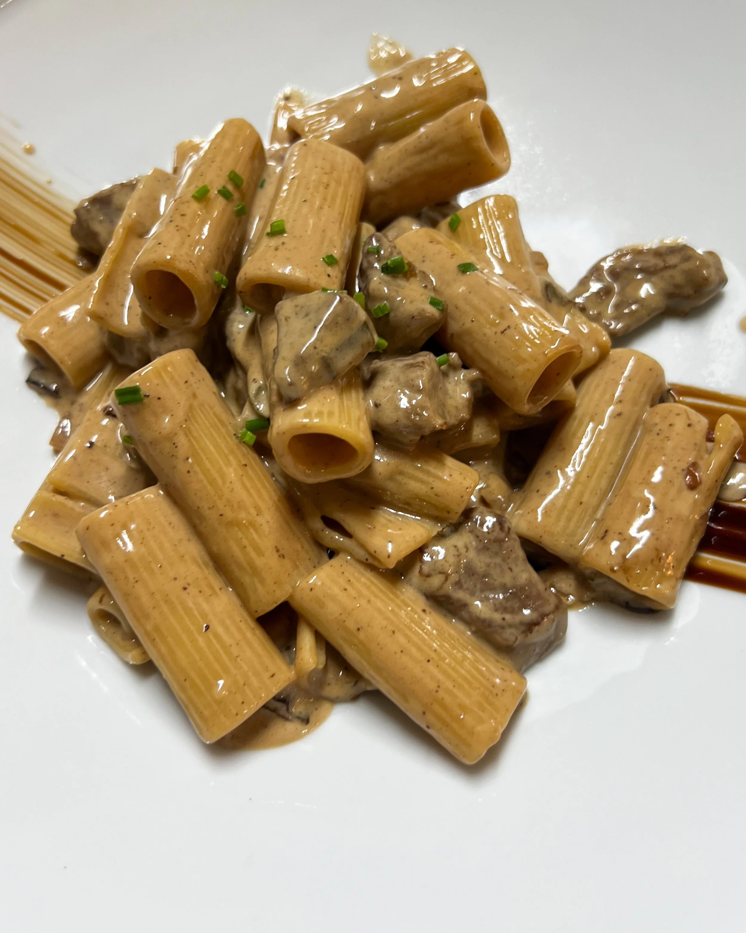 Plate of pasta with creamy sauce, pieces of meat, and garnished with chopped chives.