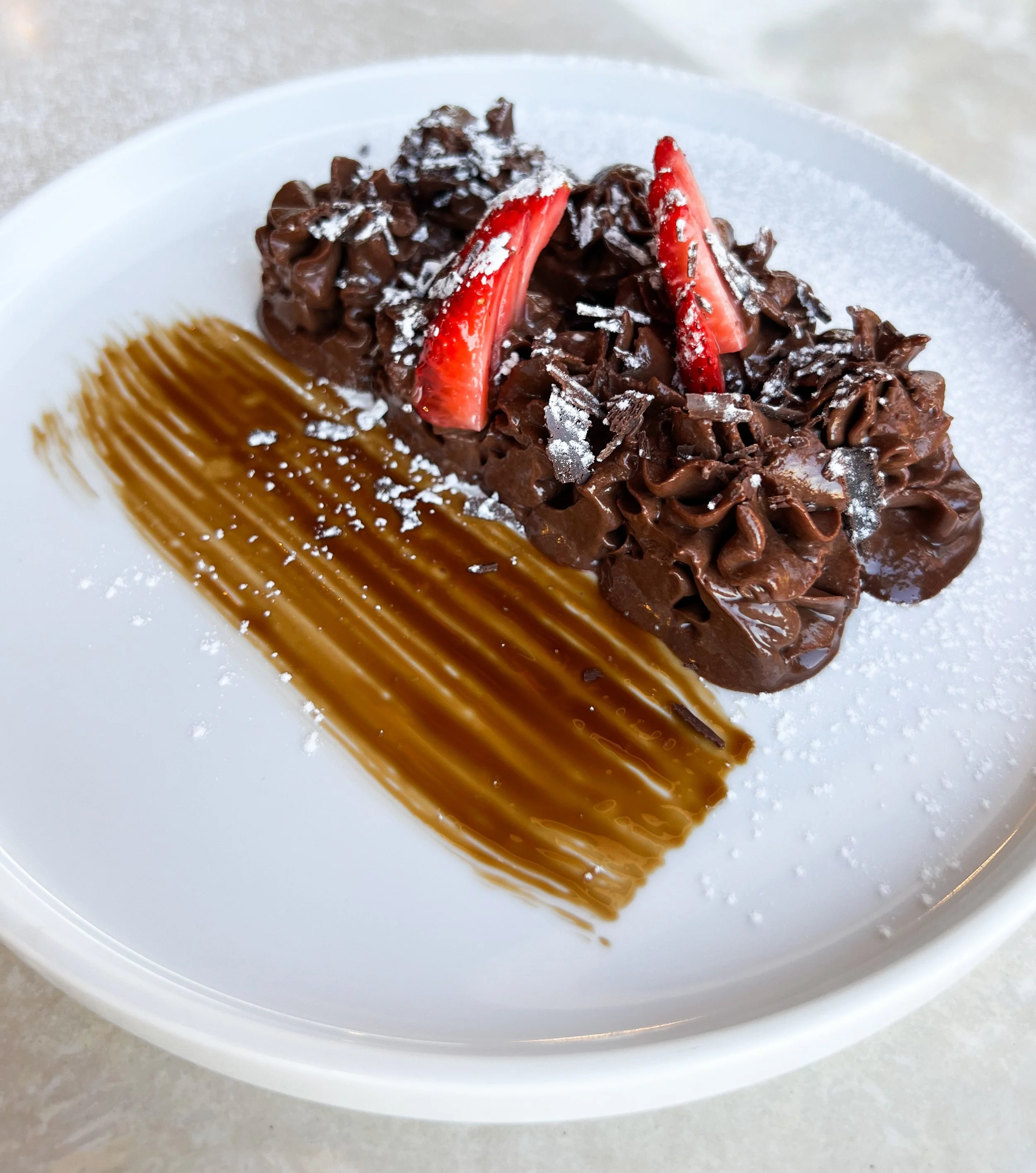 Chocolate dessert with sliced strawberries and edible silver flakes, garnished with a caramel sauce streak on a white plate.