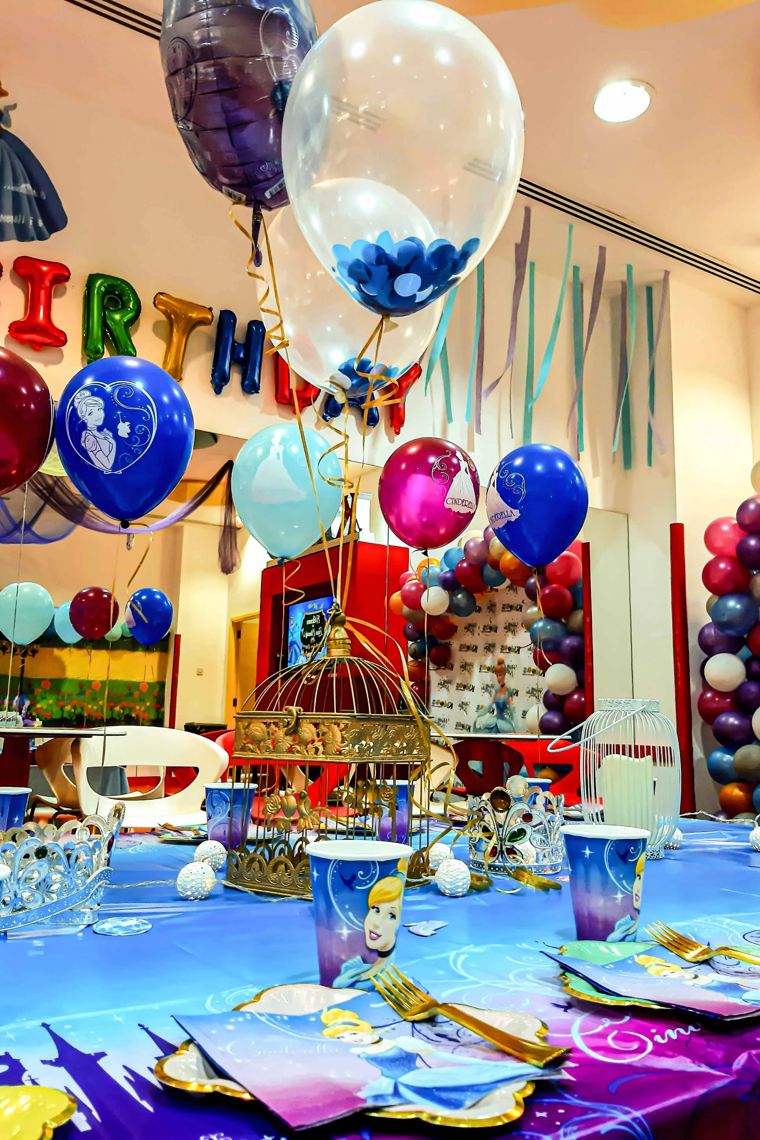 A colorful children's birthday party decorated with balloons, themed tableware featuring a princess, and a backdrop with balloons and streamers.