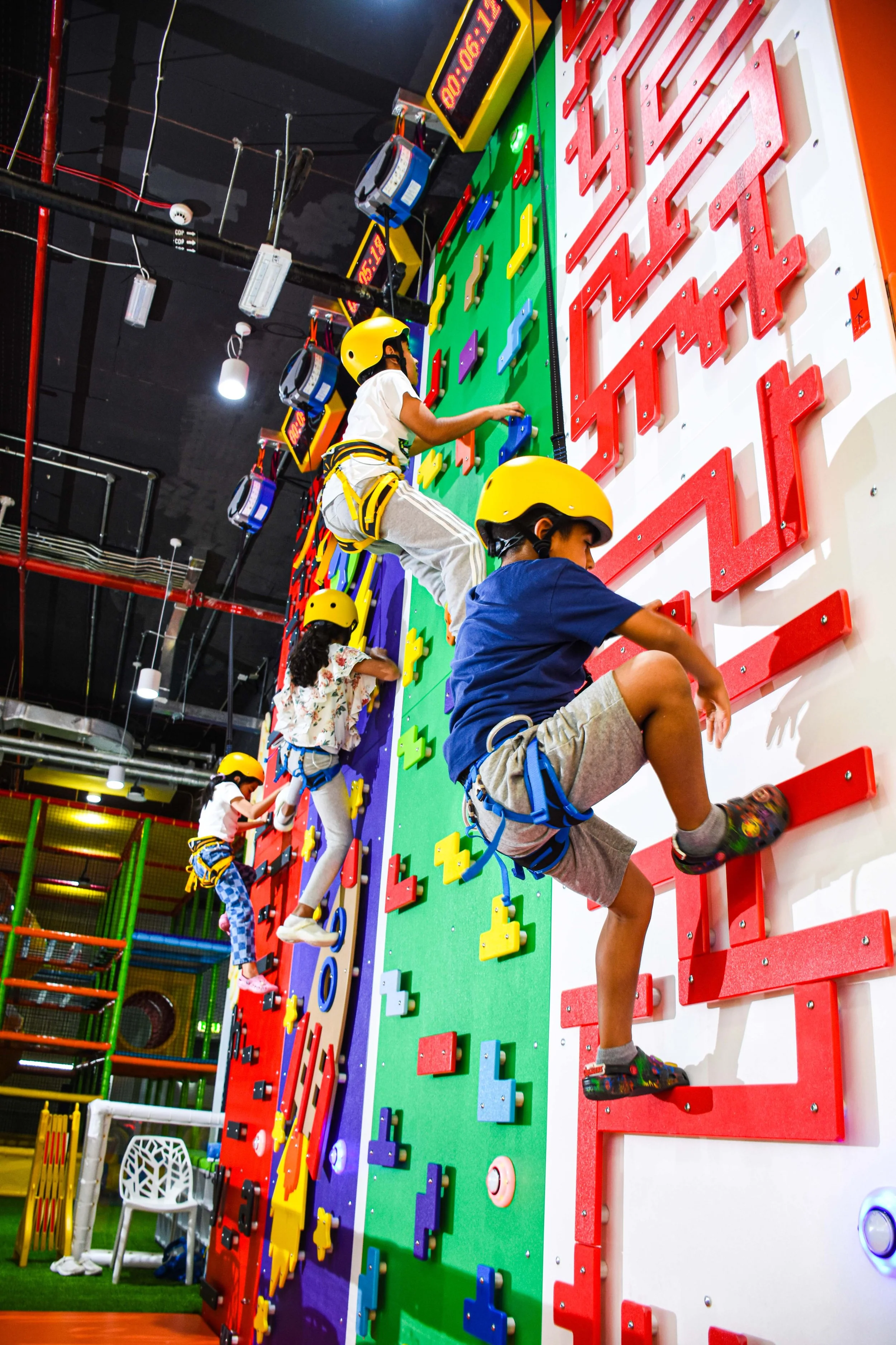 Kids wearing yellow safety helmets climbing an indoor rock climbing wall with colorful grips.
