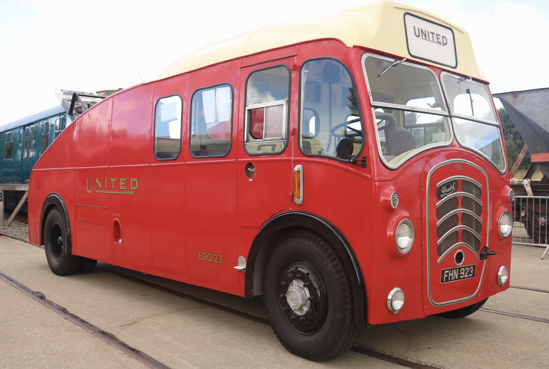 A vintage red bus with a cream-colored roof, labeled 'United' on the front and side, parked on railway tracks.
