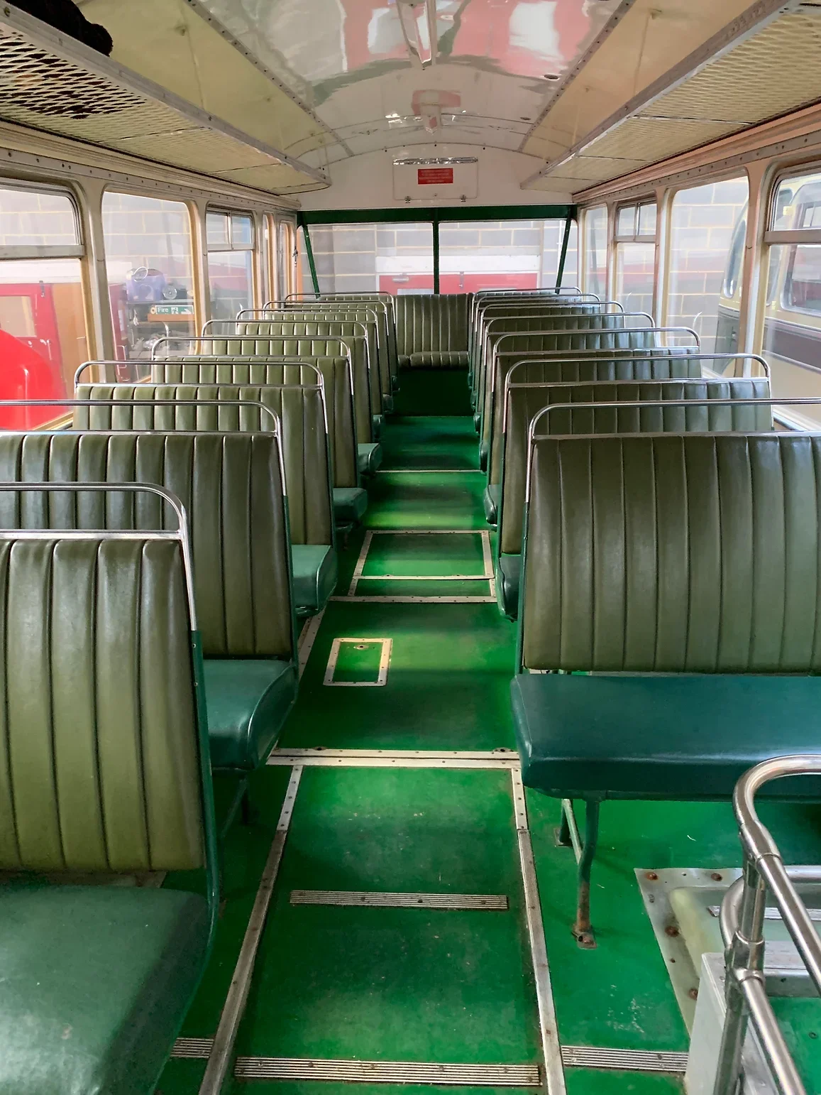 Interior of an empty vintage bus with green seats and green flooring, viewed from the front.