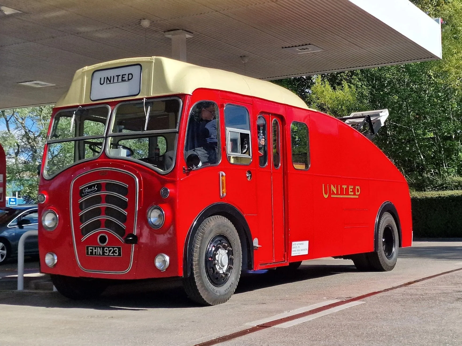 A vintage red bus with a cream-colored roof, labeled 'United' on the front and side, parked on railway tracks.