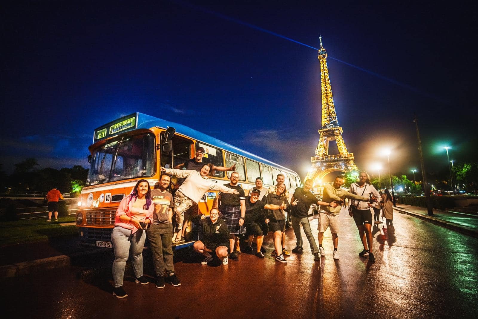 A group of people posing in front of a vintage bus and the Eiffel Tower illuminated at night.