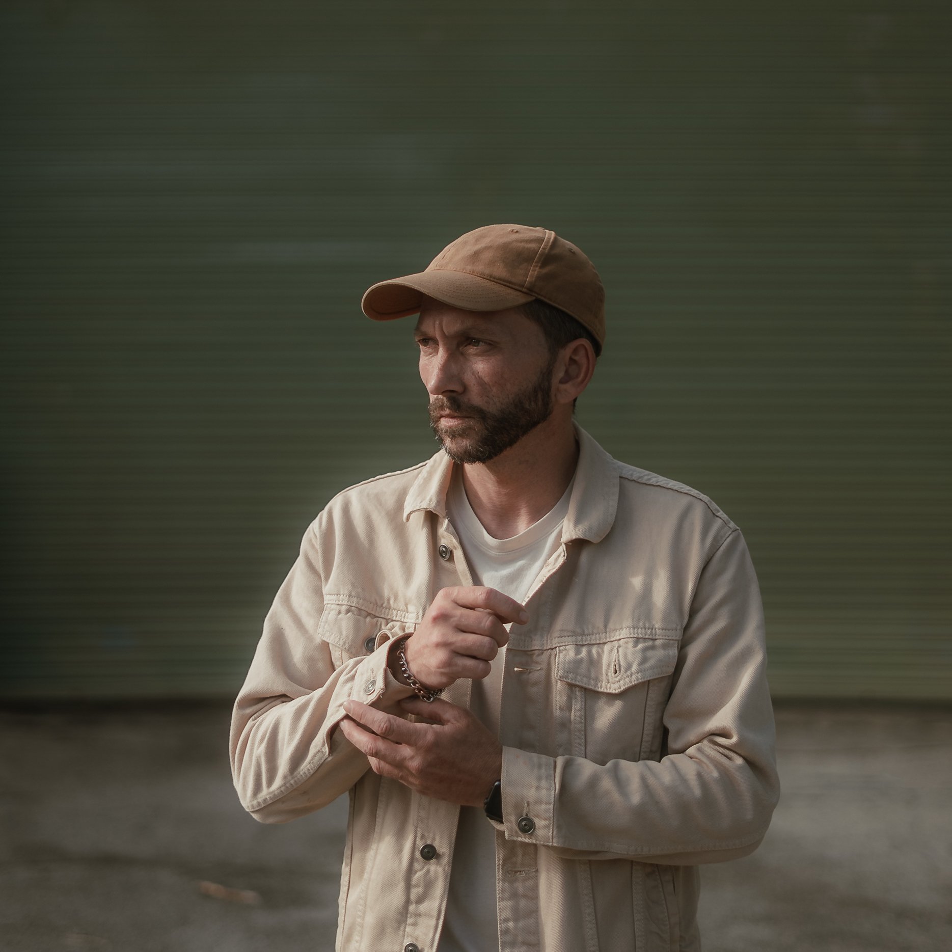 Jake Rhodes wearing a tan cap and beige jacket, standing outdoors with a blurred green background.