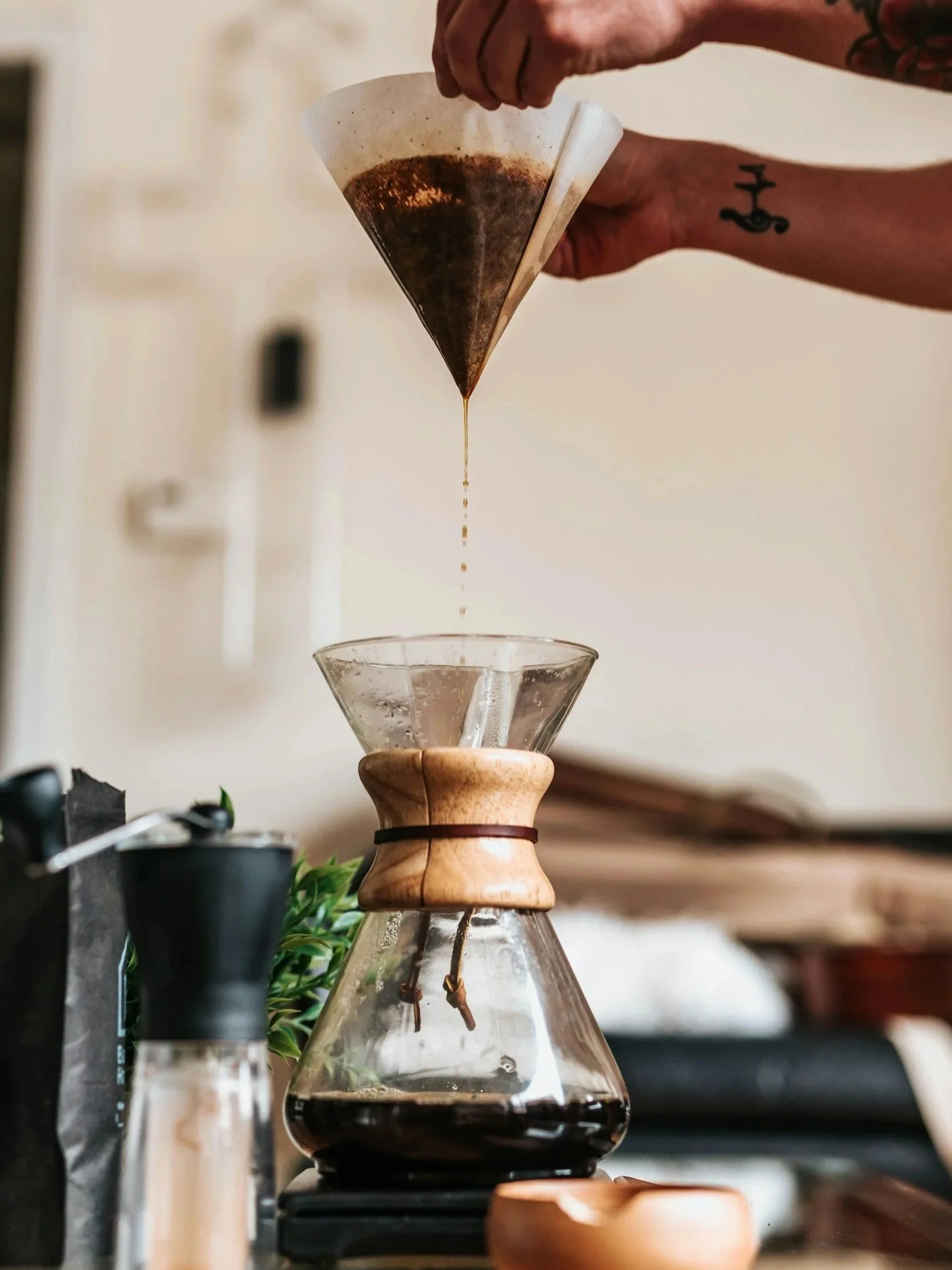 Person brewing coffee using a chemex with a cone-shaped filter and glass dripper.