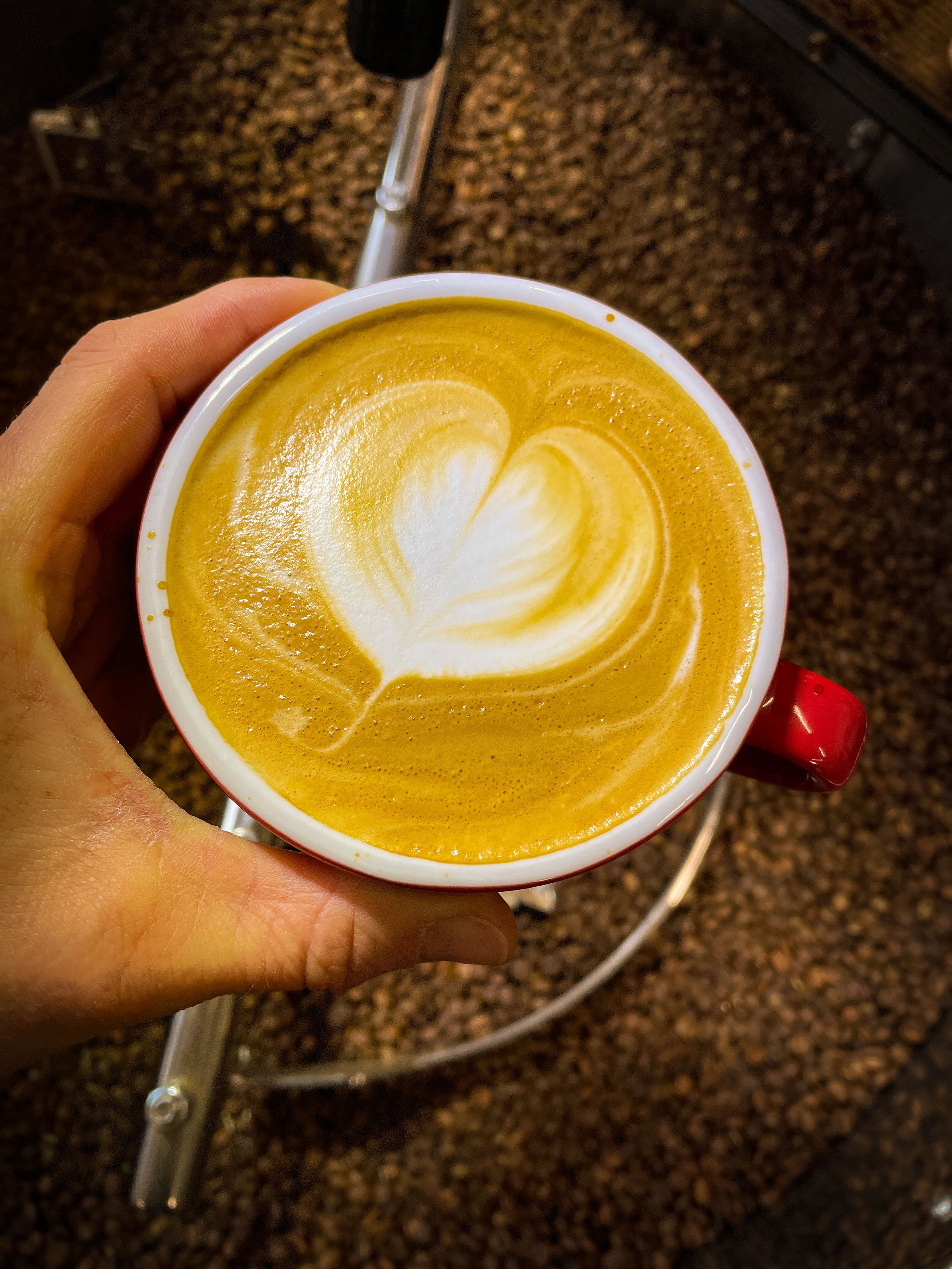 A person holding a red mug with a latte art heart design on top of a flat white coffee