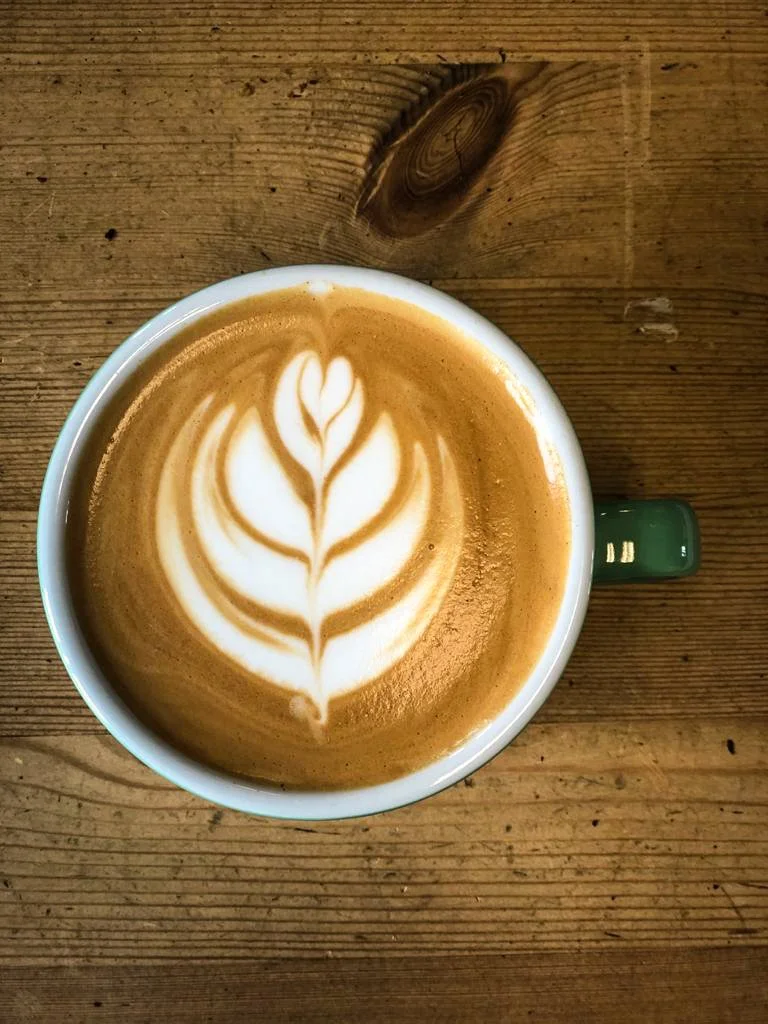 A cup of coffee with a heart-shaped latte art design on top, placed on a wooden table.