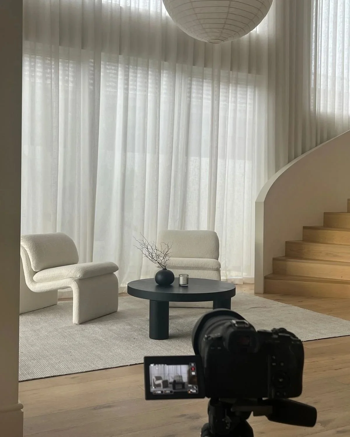 A wall decorated with nine framed pictures in gold and brown frames arranged in a 3x3 grid, with a small sideboard below holding a black vase with green leaves, a round clock, and three gold and black striped vases.