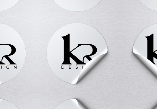 White circular stickers with a black logo and text, partially peeled at the edges, on a light gray surface.