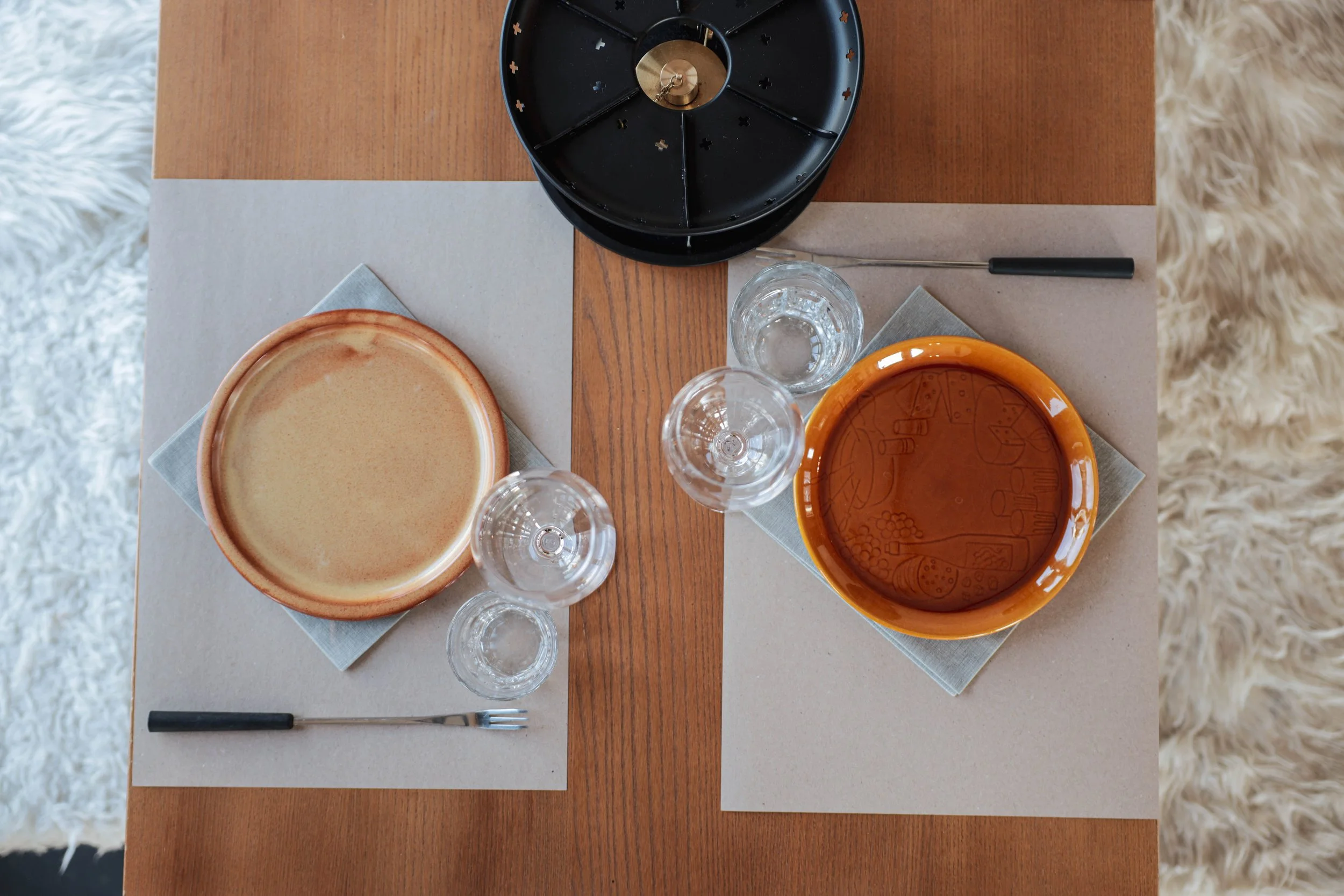 Zwei Teller auf einer Esstafel mit Getränken, Besteck und einem schwarzen Teller in der Mitte.