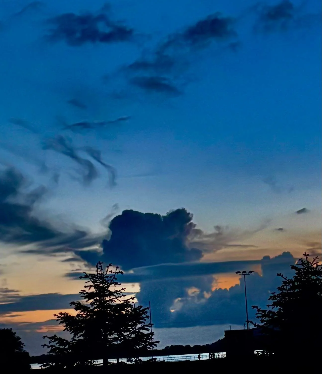 Sky at dusk with dark clouds and silhouettes of trees and a railing in the foreground.