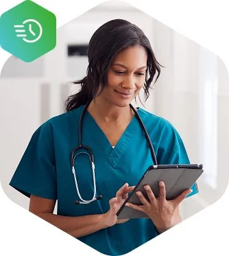 A female healthcare professional in scrubs holding and looking at a tablet device.