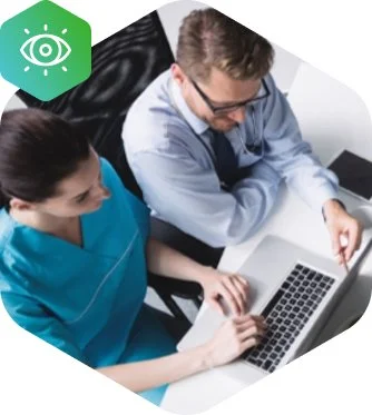 Two medical professionals, a man and a woman, looking at a laptop together, in a clinical setting.