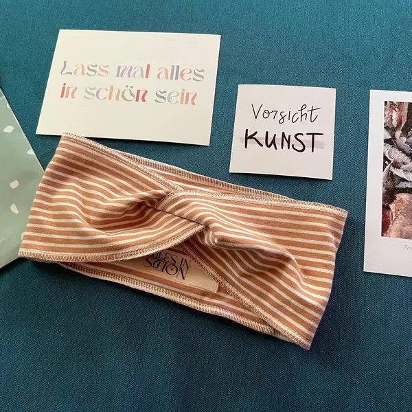 Zwei Notizzettel mit deutschen Sprüchen, ein gestreifter Kopfbedeckung und ein Bild auf einer blauen Oberfläche.