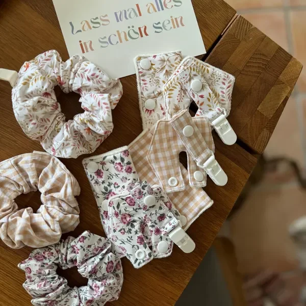Haaraccessoires mit Blumen- und Karomustern und einem Schild mit der Aufschrift 'Lass alles in schön sein' auf einem Holz-Tisch.