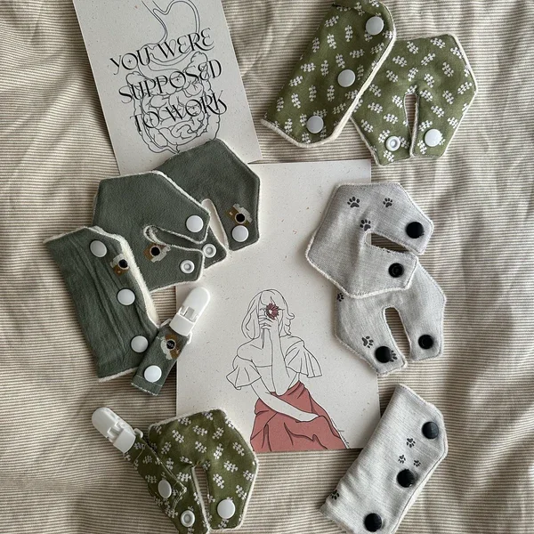 Verschiedene wiederverwendbare Stoffbinden in grau, grün und weiß mit unterschiedlichen Mustern, auf einem Stoffbett. In der Mitte ein handgezeichnetes Bild einer Frau, die eine Blume im Gesicht hält, und ein Ausdruck mit der Aufschrift 'You Were Supposed To Grow'.