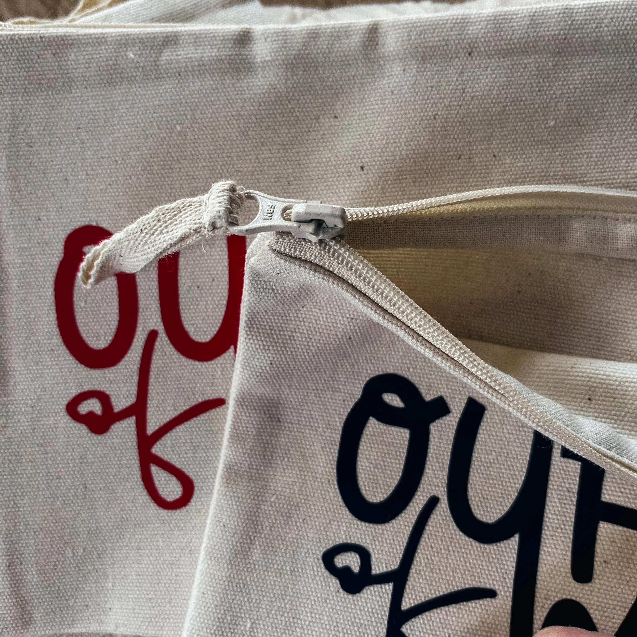 Nahaufnahme eines weißen Stoffbeutels mit rotem und schwarzem Aufdruck, sichtbar ist ein geschlossenes Reißverschlussfach.
