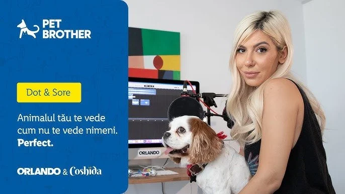 A woman with long blonde hair sitting beside a white and brown dog in front of a computer monitor. To the left, a blue and yellow graphic with logos and text in Romanian related to pet health, featuring a small dog icon and a background of the flag of Portugal.