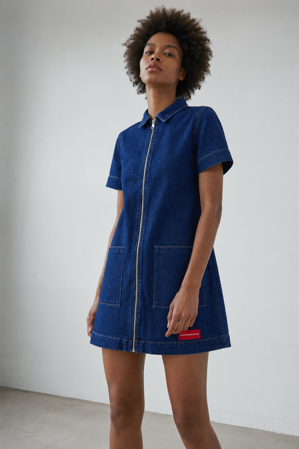 Calvin Klein Jeans women’s dark blue denim zip-front mini dress with short sleeves and front pockets, worn by model
