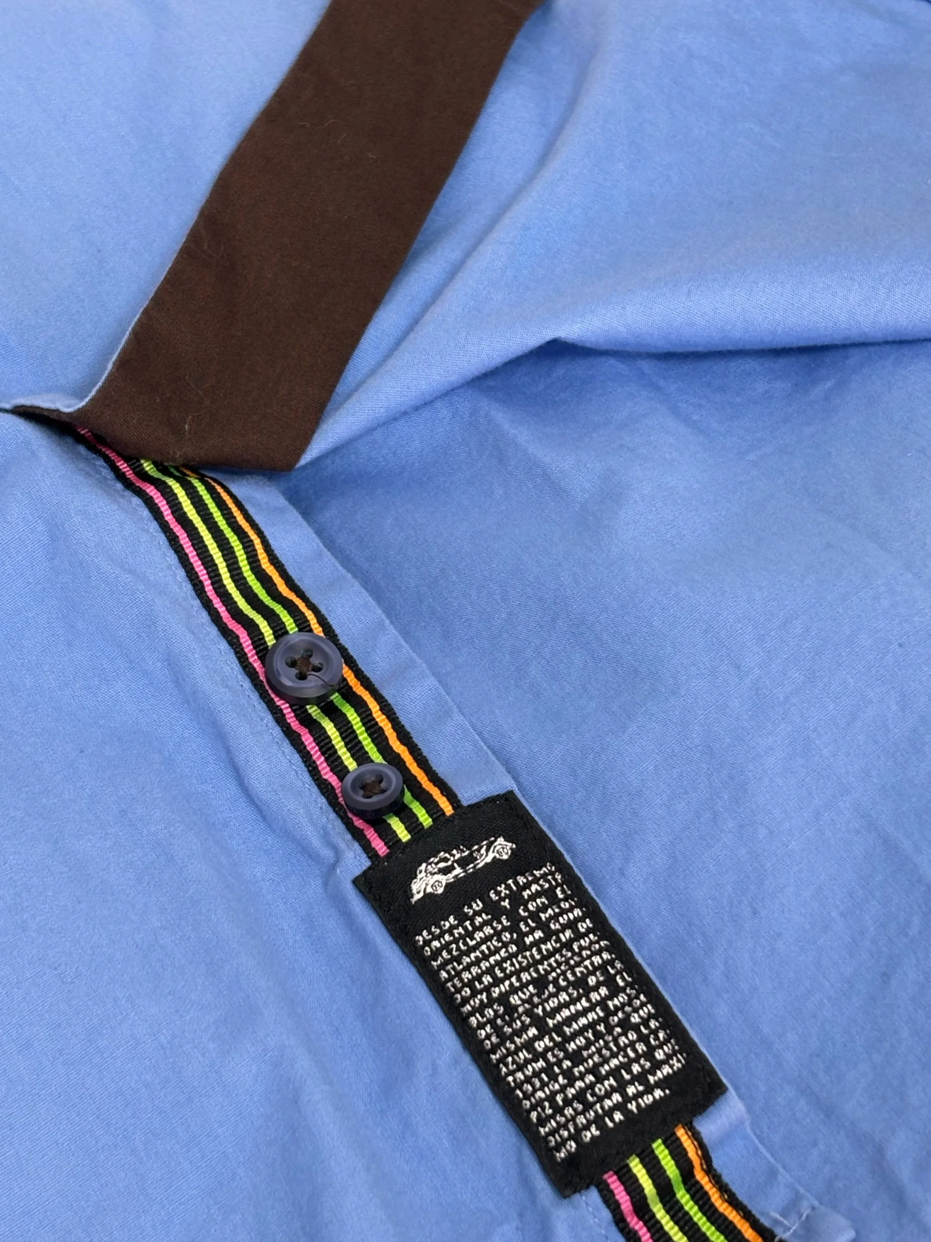 Close-up of the Dario Beltran men’s light blue shirt highlighting the multicolor striped placket tape, premium buttons, contrast brown trim and signature craftsmanship