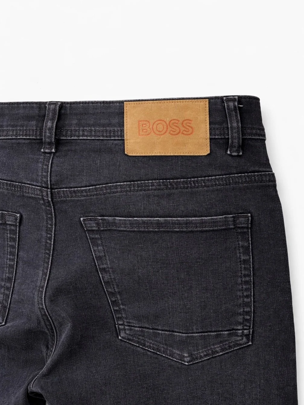 Back pocket detail of BOSS men’s dark wash designer jeans with leather logo patch and slim fit denim construction