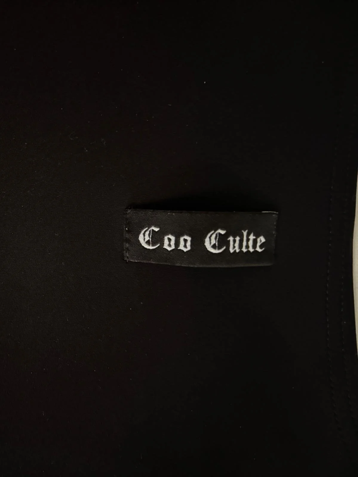 Coocult brand label detail on black women’s designer top, authentic pre-loved garment. Virtual Preview Available