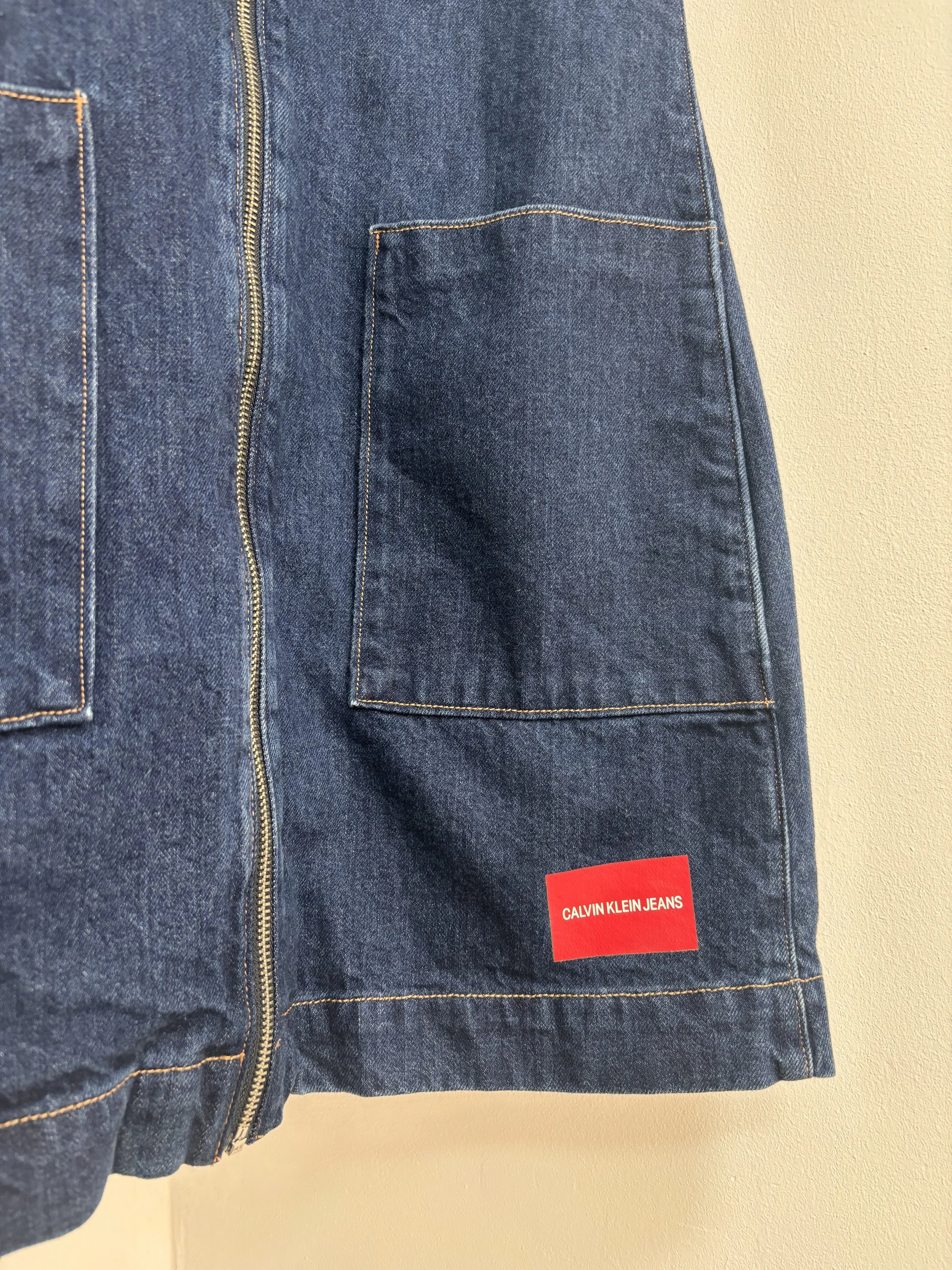Close-up of Calvin Klein Jeans red logo patch on dark blue denim dress with front pocket detail
