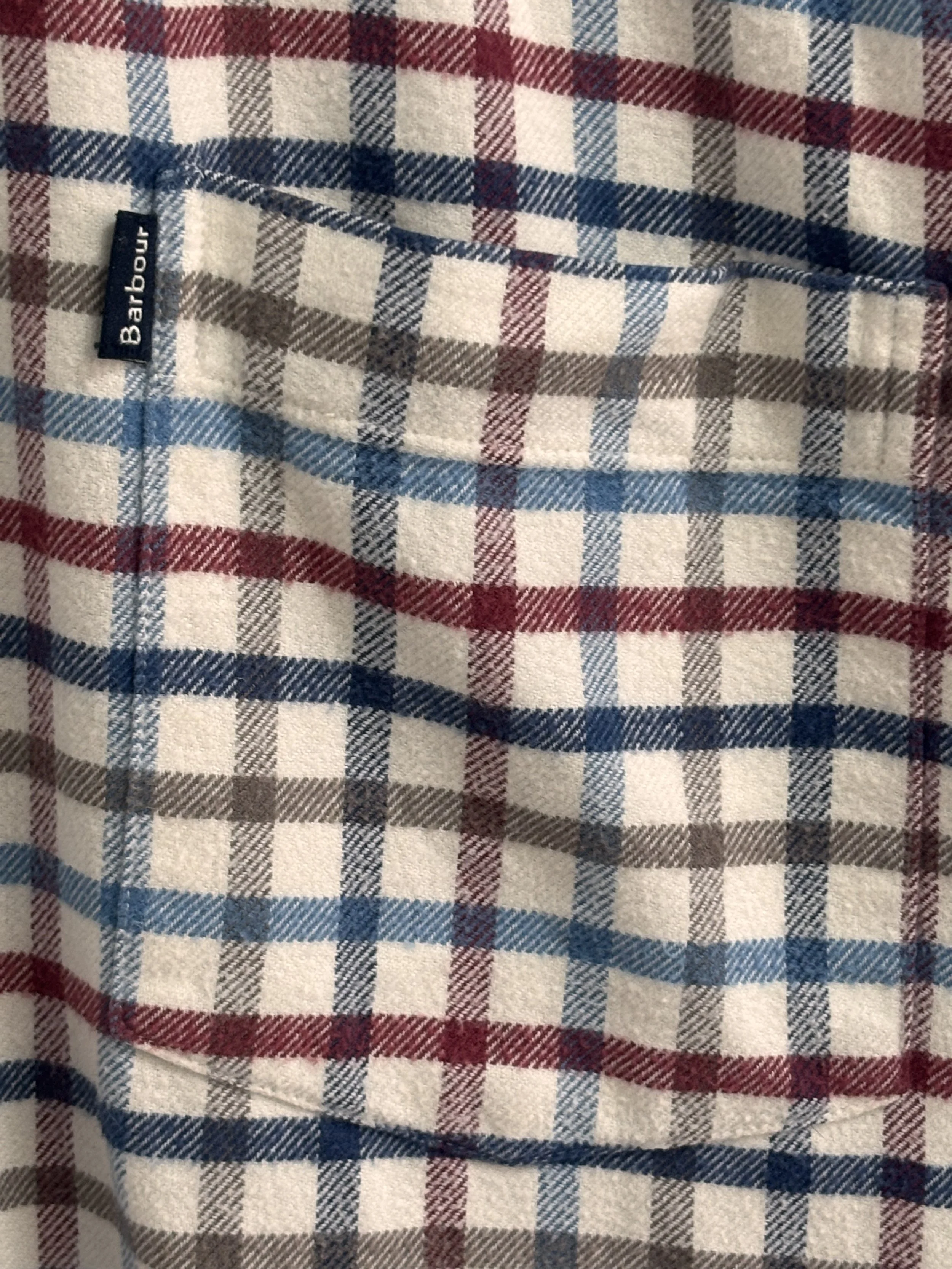 Close-up of Barbour men’s checked cotton shirt chest pocket with authentic Barbour woven logo label.
