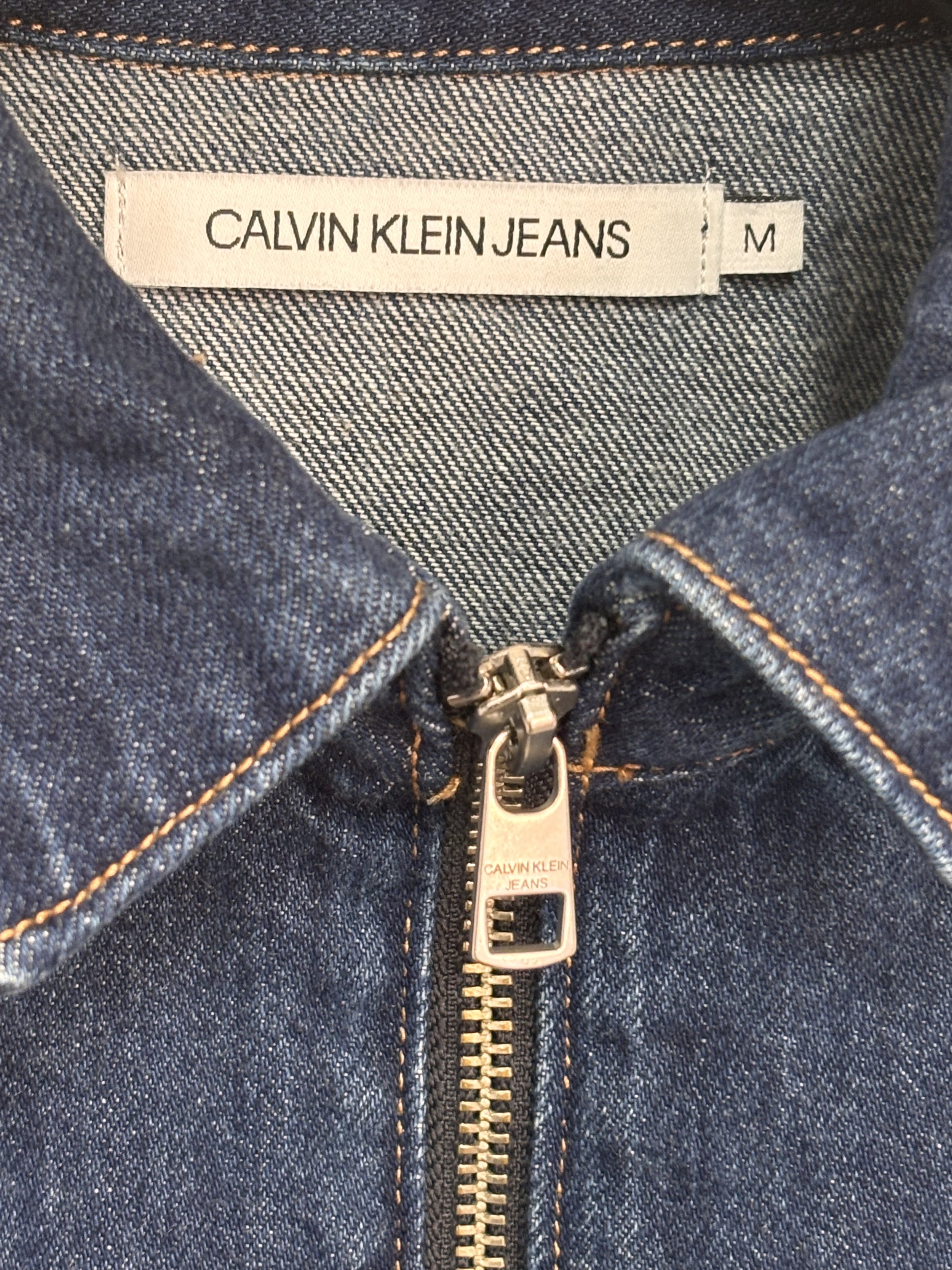 Close-up of Calvin Klein Jeans label, collar and silver front zipper on dark blue denim dress