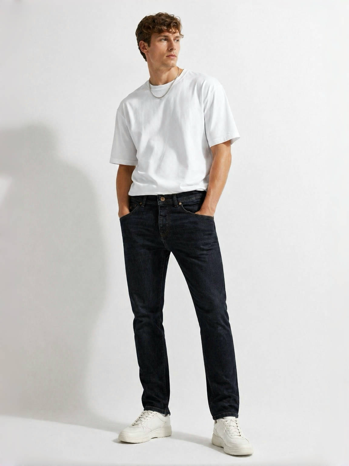 BOSS dark blue slim fit men’s designer jeans styled on model with white t-shirt and white sneakers in minimalist studio setting