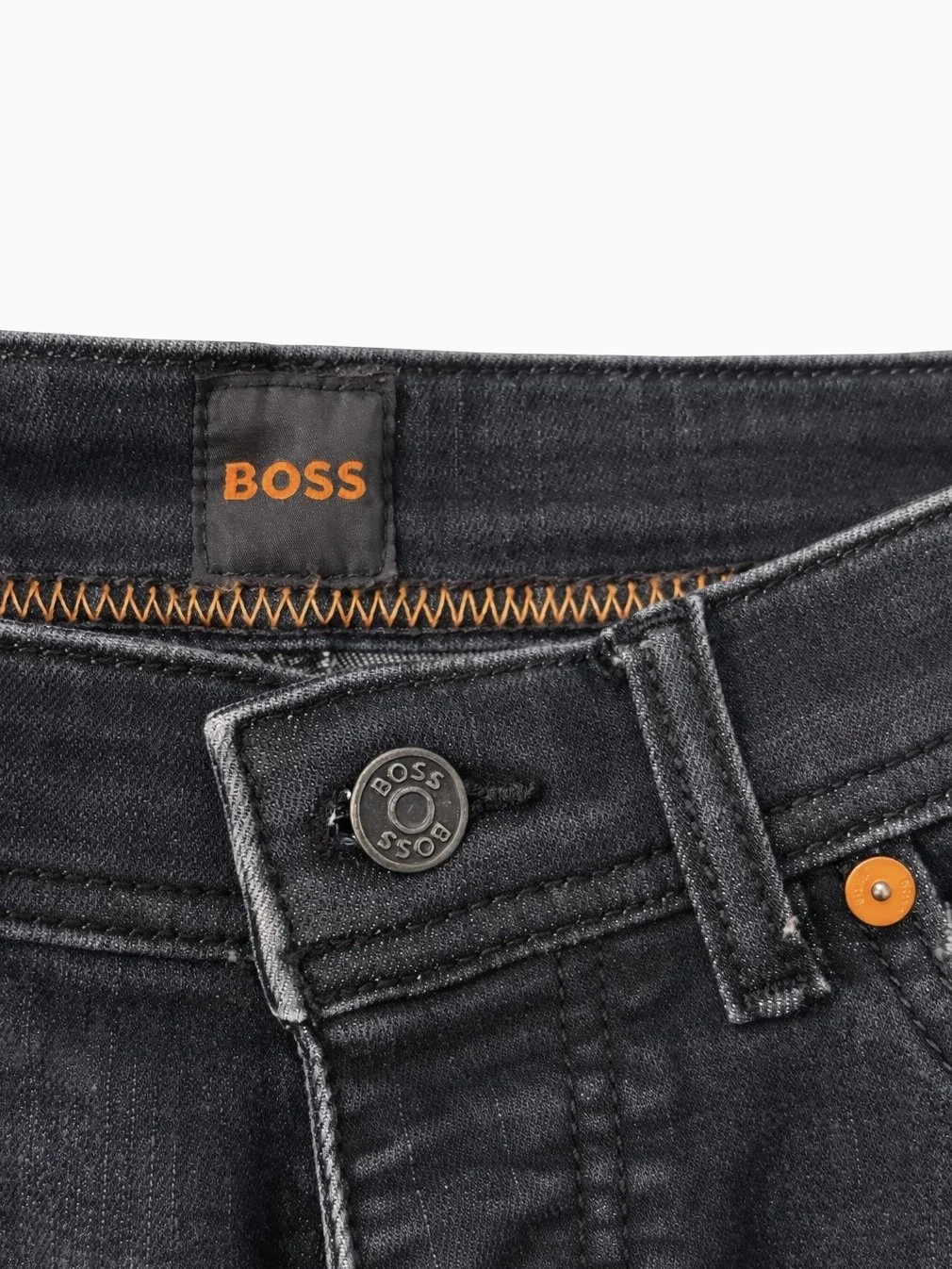 Close-up of BOSS branded button and waistband detail on dark blue luxury men’s denim jeans with faded wash finish