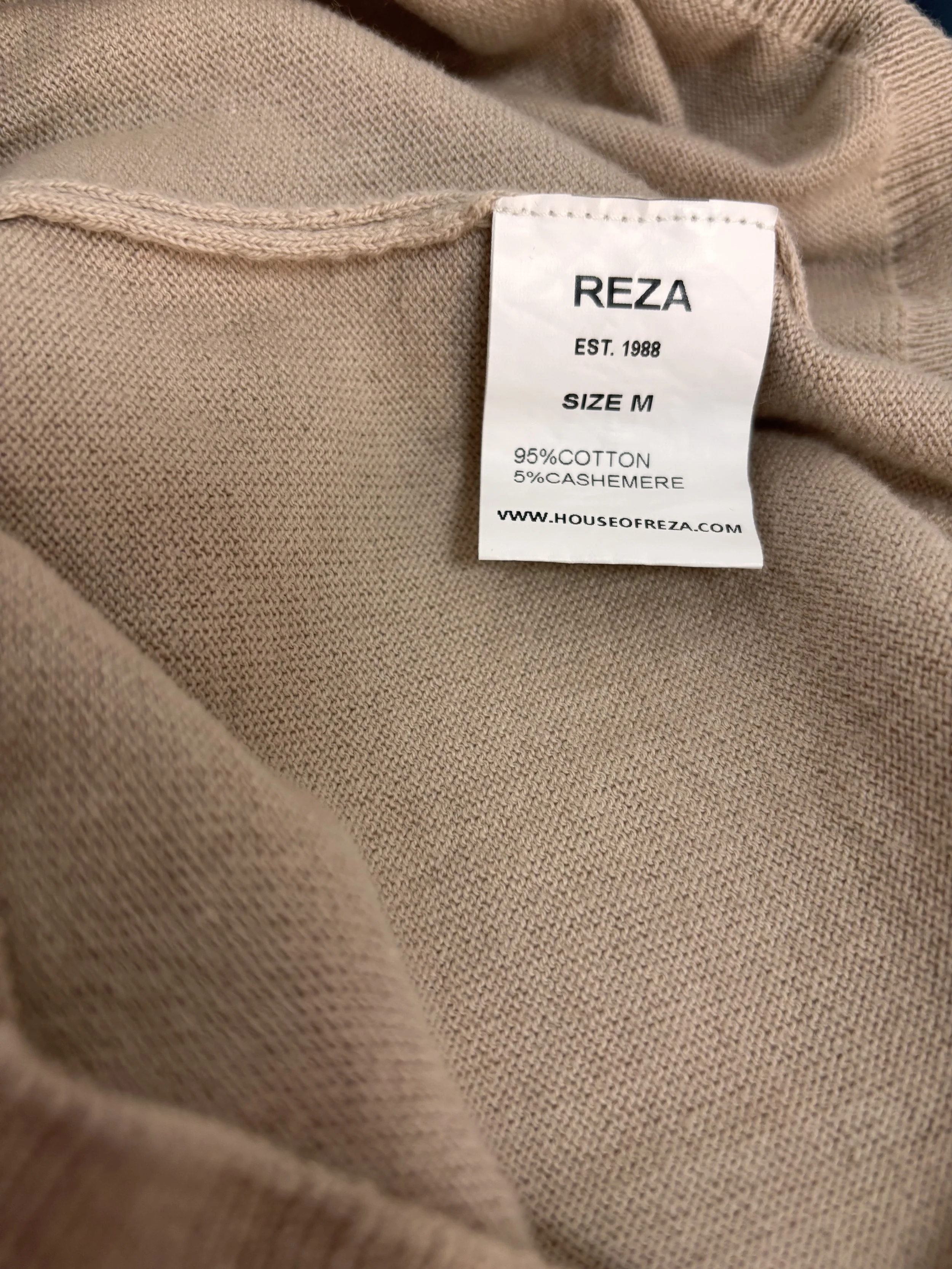 REZA size M label and fabric composition tag showing 95% cotton and 5% cashmere on a premium beige knit polo sweater.
