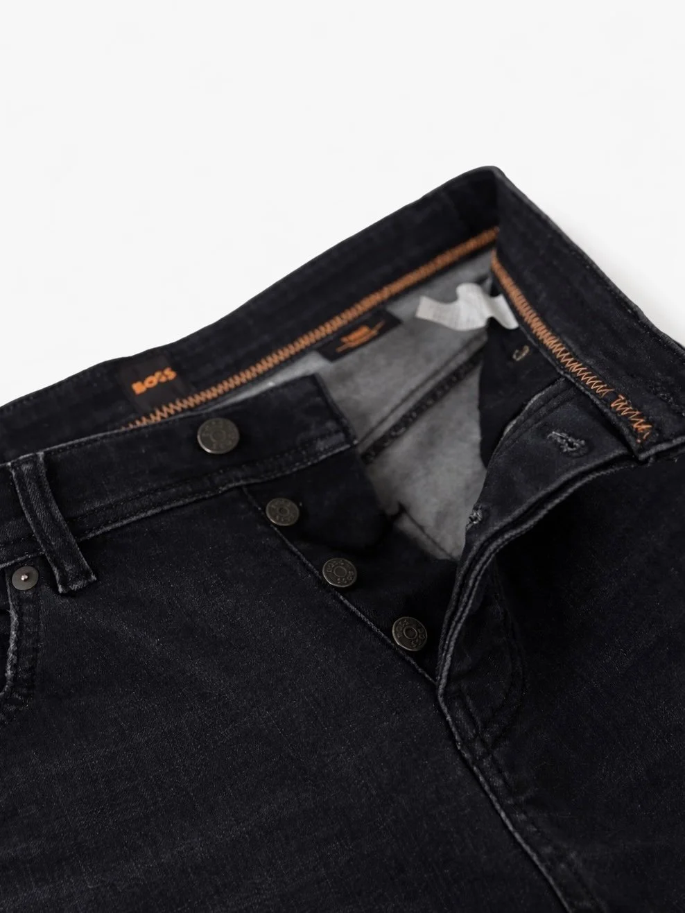 Interior button fly detail of BOSS dark blue men’s jeans with branded hardware and orange contrast stitching