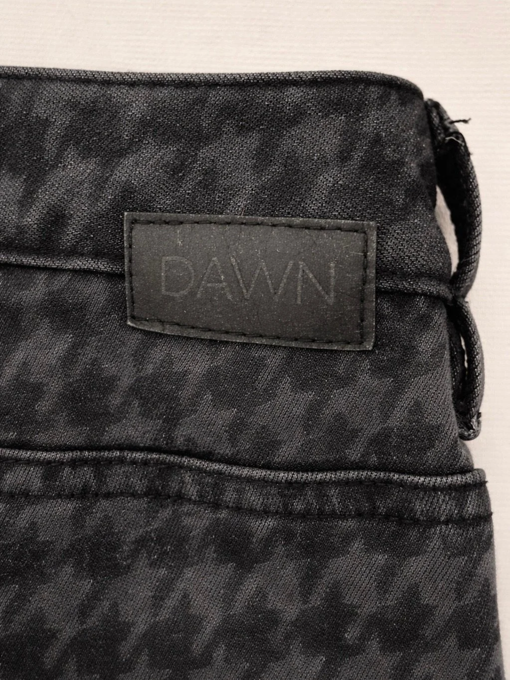 Close-up of DAWN black houndstooth jeans back logo patch and denim texture