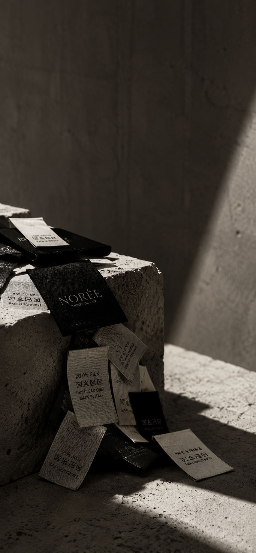 Minimalist still life of designer garment labels and care tags in a brutalist setting, symbolizing craftsmanship, timeless fashion and luxury pre-owned designer pieces curated by Norée.