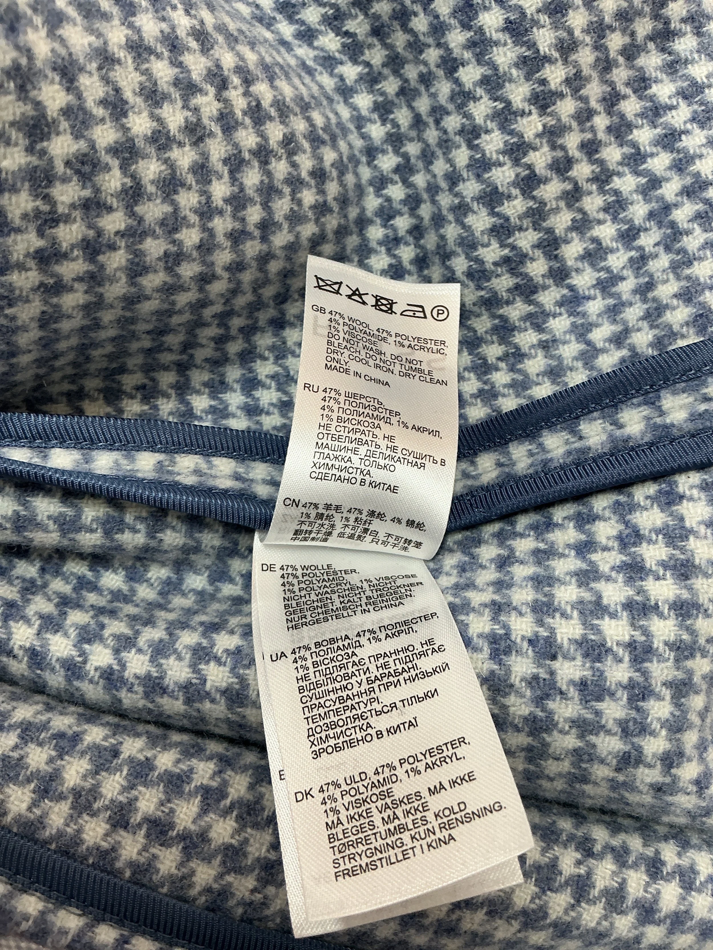 Close-up of Reiss men’s blue houndstooth overshirt care label showing wool blend fabric composition and garment care instructions.