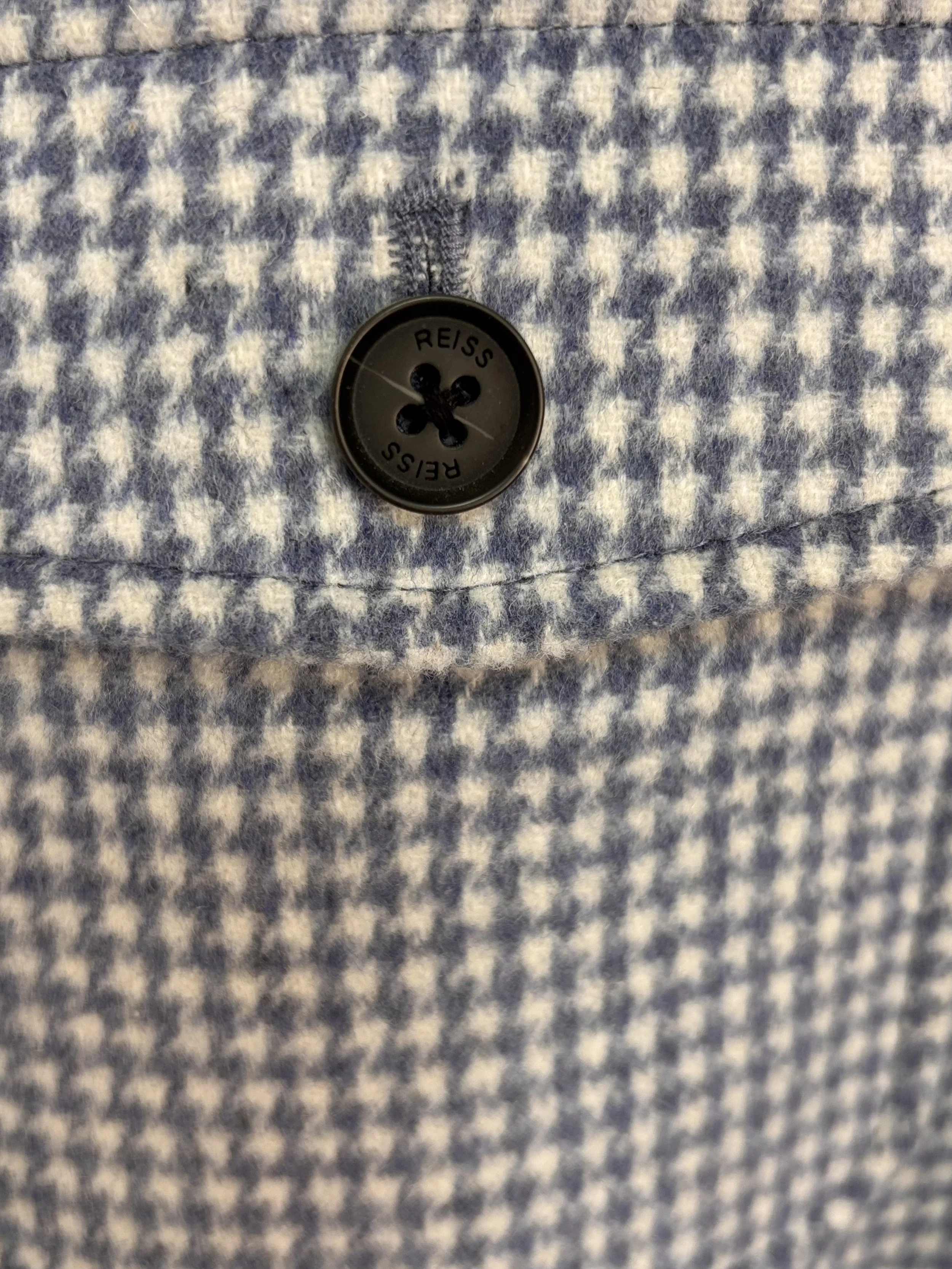 Close-up detail of Reiss branded button on blue and ivory houndstooth wool blend overshirt with premium textured fabric.