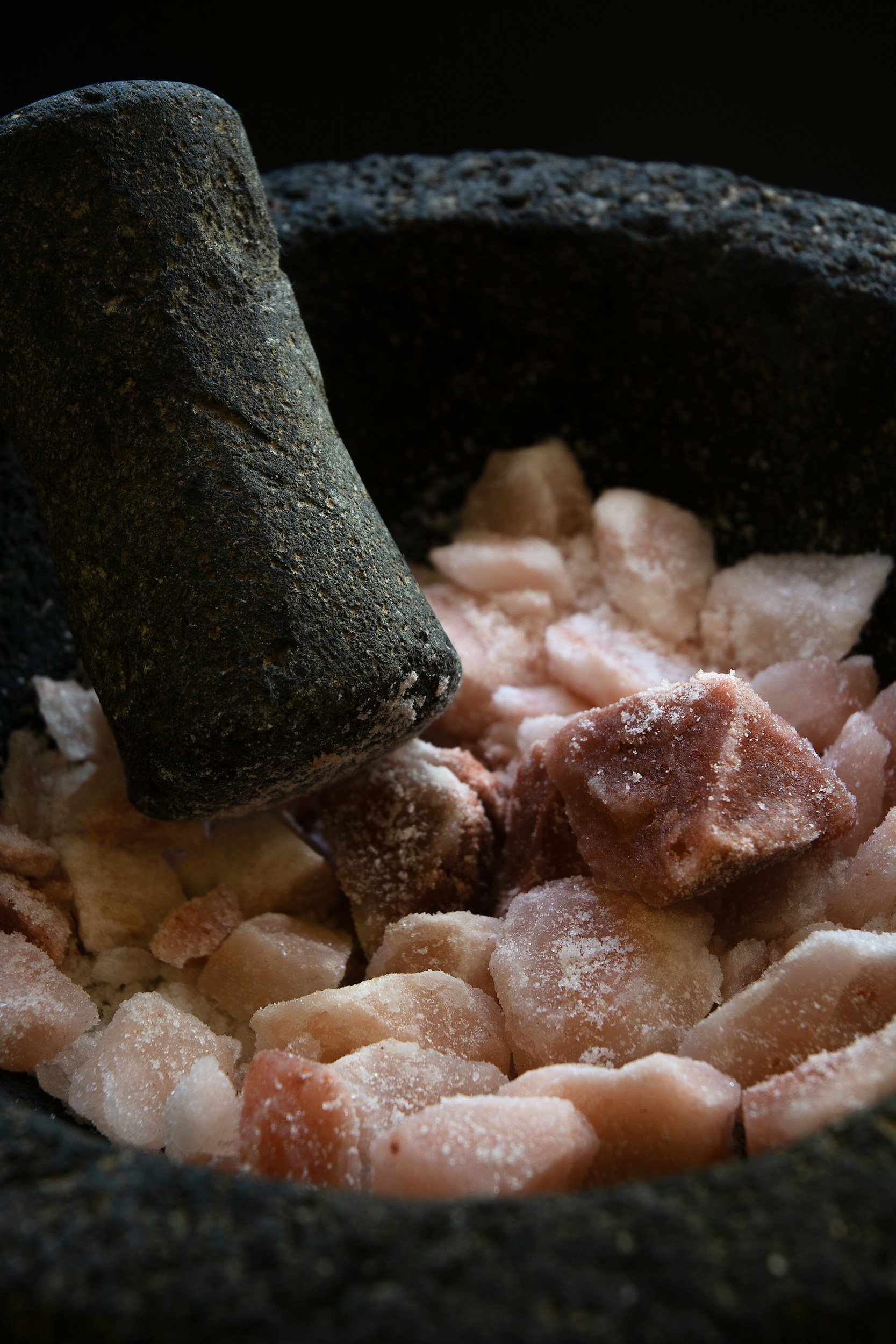 Close-up of a black stone mortar and pestle with pink Himalayan salt and dried herbs inside