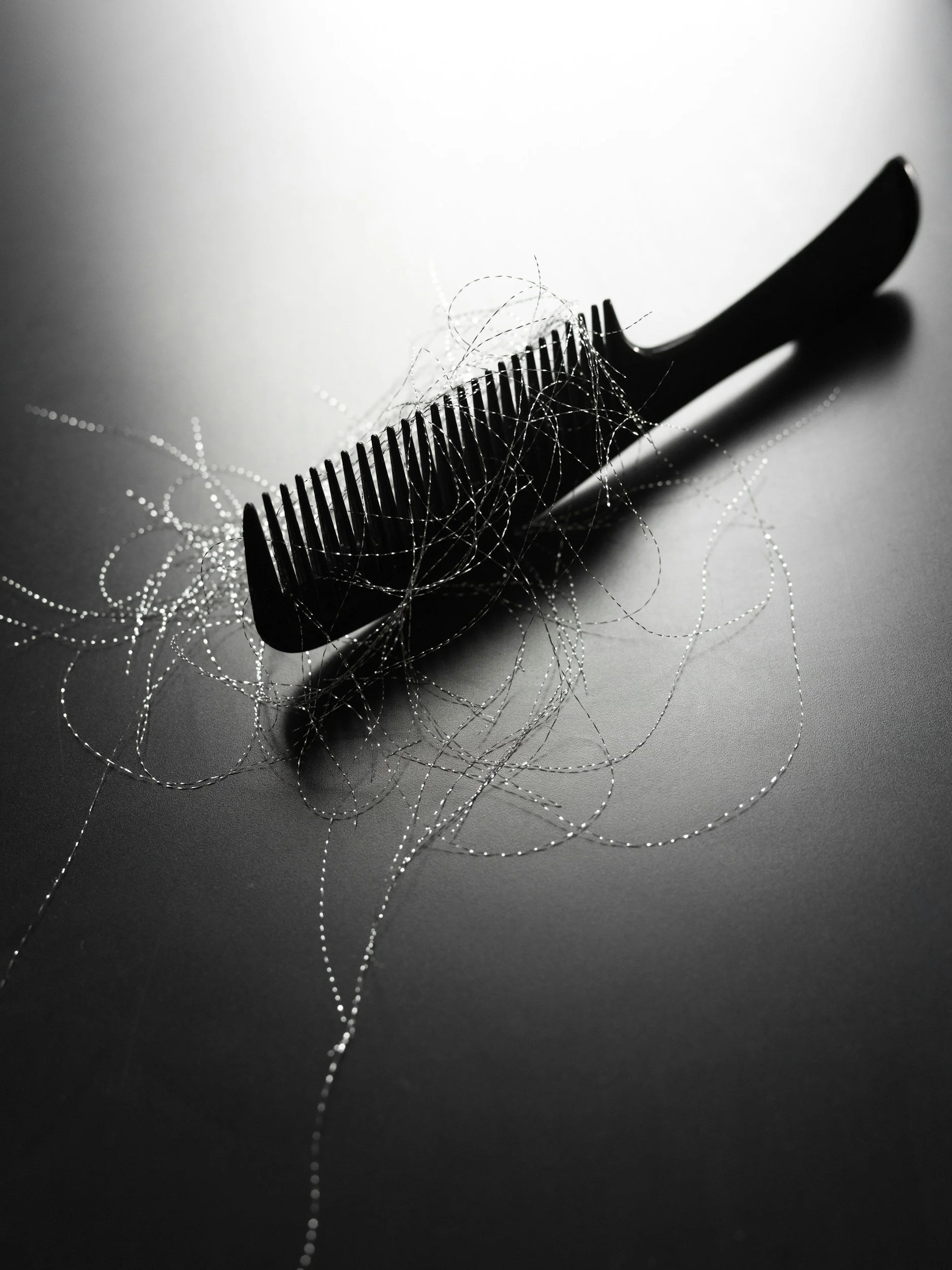 A black hair comb tangled in silver hair (or thread) on a smooth surface.