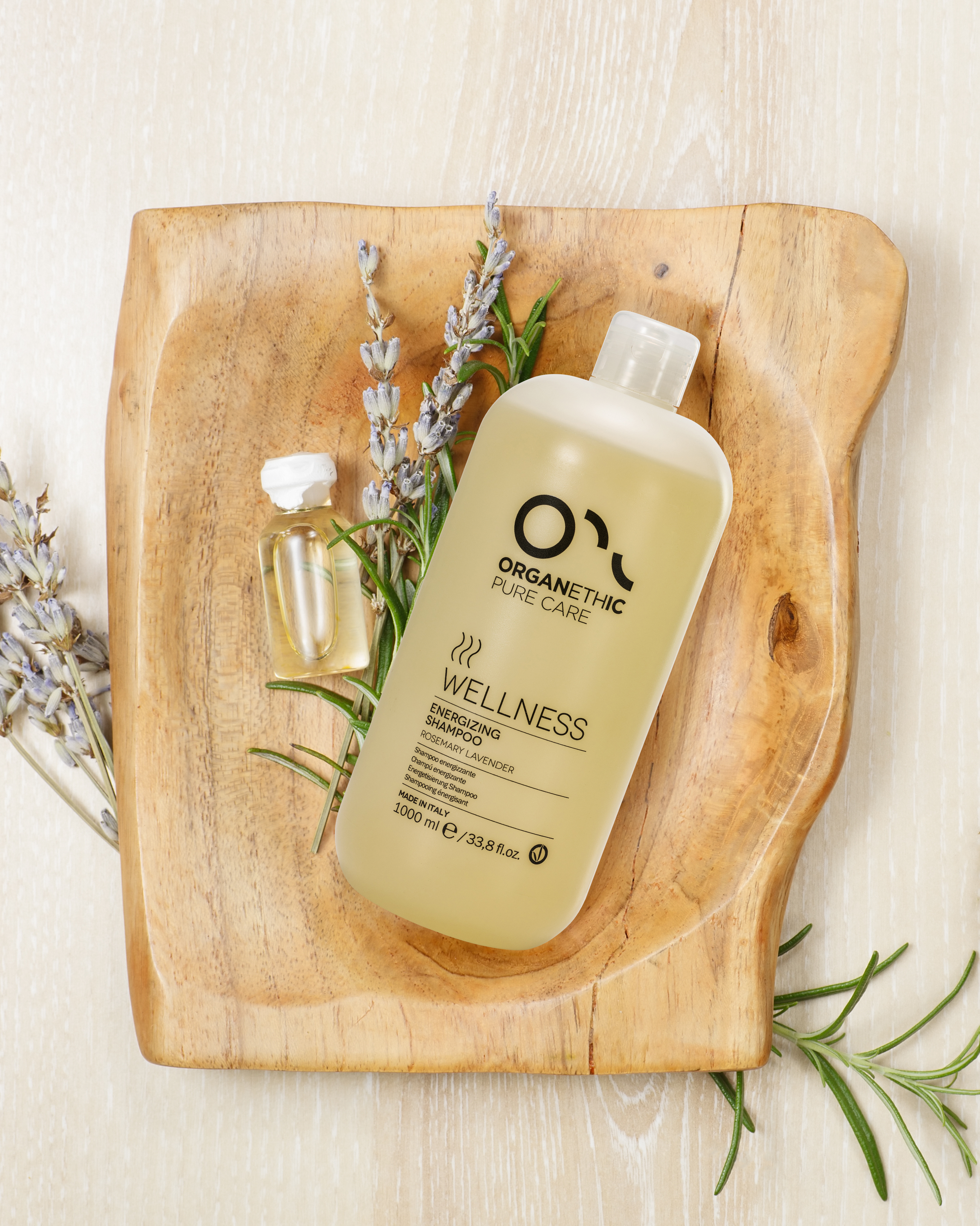 A bottle of Organethic Wellness Energizing Shampoo with lavender and rosemary, placed on a wooden tray along with lavender flowers and a small vial of oil.